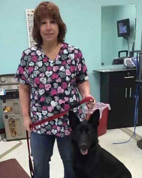 Terri Miller, owner and groomer, standing with a black German Shepherd